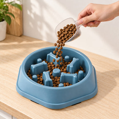 Hand pouring kibble from a clear scoop into the blue bowl on a wooden counter