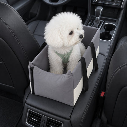 White fluffy dog in green harness sitting upright in the grey car seat box on the console