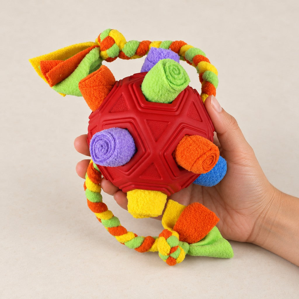 Hand holding the red snuffle ball with fleece rolls in its openings and braided rope loop