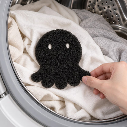 Hand holding the black foam octopus on white laundry inside a washing machine drum