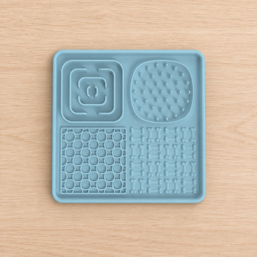 Square pale blue lick mat with four textured zones, shown top-down on a wooden surface