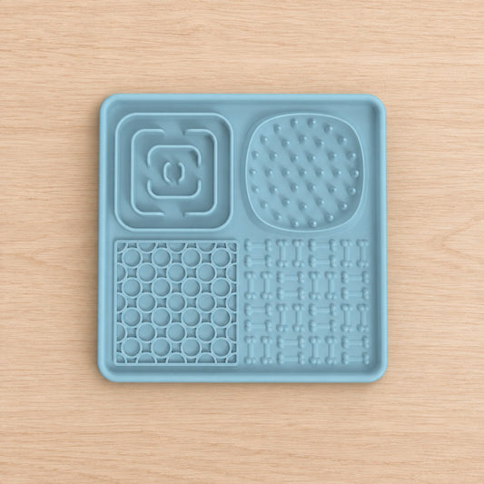 Square pale blue lick mat with four textured zones, shown top-down on a wooden surface