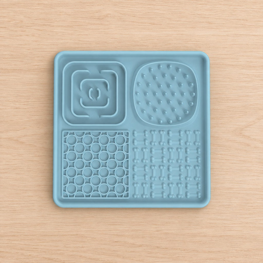 Square pale blue lick mat with four textured zones, shown top-down on a wooden surface