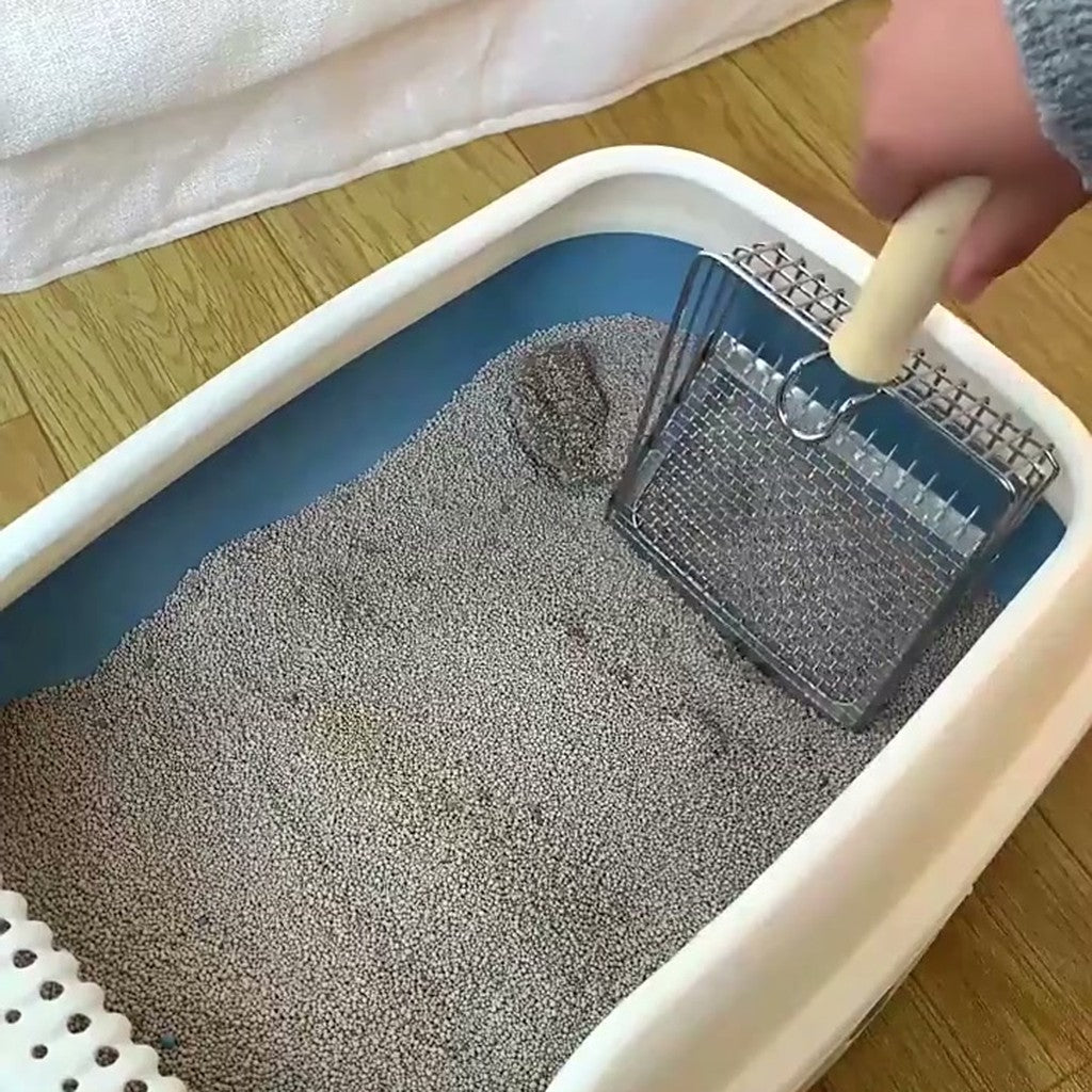 Hand holding the mesh scoop upright above a litter tray, other hand open beside it