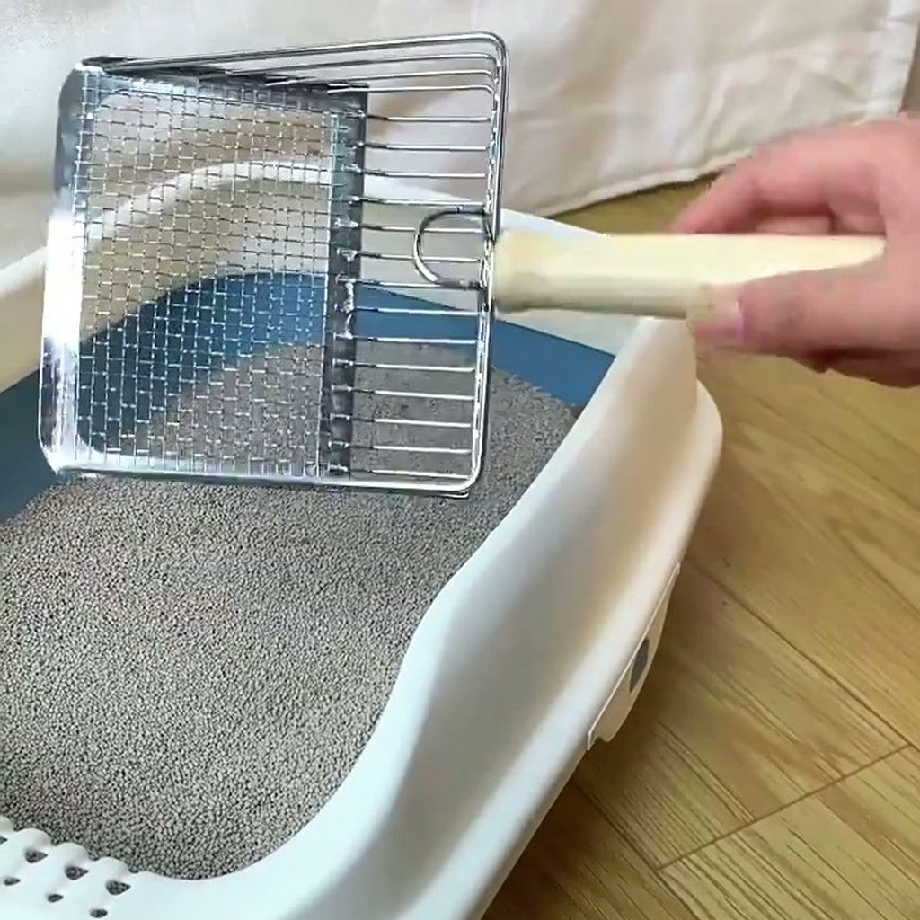Hand holding the mesh scoop inside a white litter tray filled with grey litter