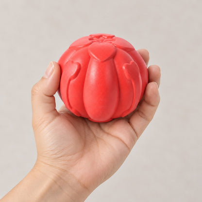 Hand holding the red ribbed ball with heart-shaped details against a plain background